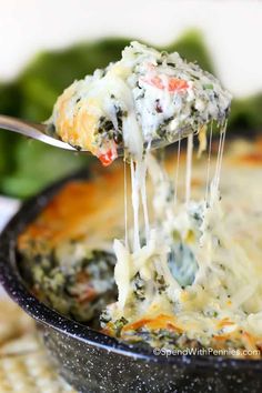 a spoonful of cheese ranch spinach dip is being lifted from the casserole dish