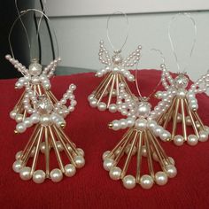 three gold and white angel ornaments on a red cloth with silver wire attached to them