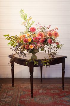 a table with flowers on it sitting in front of a white wall and red rug