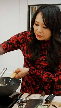 a woman cooking food in a wok on top of a kitchen counter with utensils