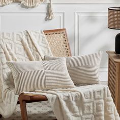 a white blanket sitting on top of a wooden chair next to a table with a lamp