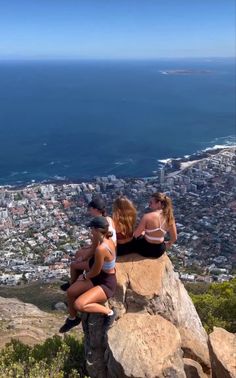 two women sitting on top of a rock with the ocean in the backgroud