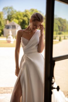 a woman in a white dress standing by a window