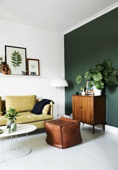 a living room with green walls and white flooring is pictured in this image, there are plants on the wall next to the couch