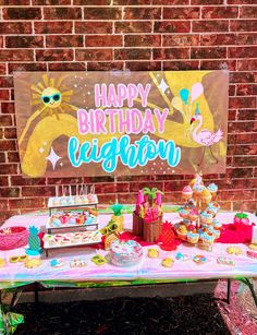 a birthday party with cake, cupcakes and candy on a table in front of a brick wall