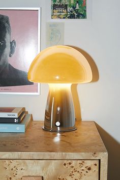 a table lamp sitting on top of a wooden dresser next to a painting and books