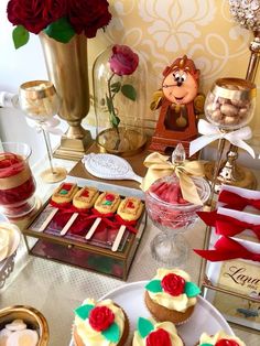 a table topped with lots of cupcakes covered in frosting and red roses