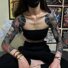 a woman wearing a black mask sitting on top of a bed next to a wall covered in tattoos