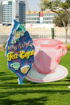 a pink tea cup sitting on top of a green field next to a large sign