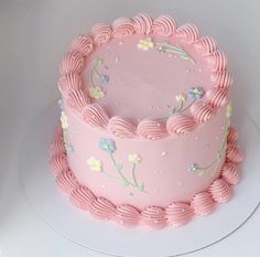 a pink frosted cake with flowers and swirls on it's side sitting on a white plate