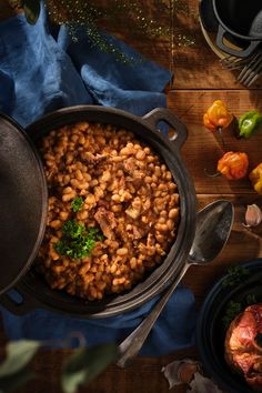 a pot filled with beans and vegetables on top of a wooden table next to utensils