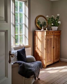 a wooden cabinet sitting in the corner of a living room next to a window with potted plants on top of it