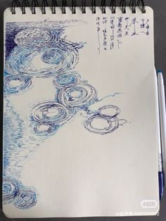 a spiral notebook with an ink drawing of water and circles on the cover, next to a pen