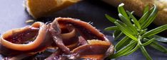 slices of meat on a plate next to bread and green sprig of rosemary