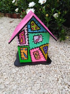 a colorful birdhouse sitting on top of gravel next to some white and pink flowers