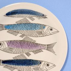 three fish on a white plate with blue and pink stripes in the center, against a light blue background