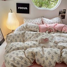 a bed with pink sheets and pillows in a bedroom next to a round window that reads focus