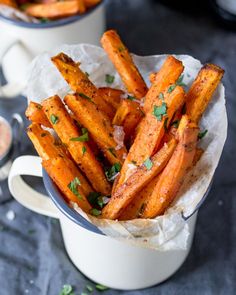 baked sweet potato wedges with parsley on top in a white bowl next to two mugs