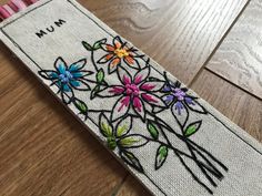 a pencil case with flowers painted on the side and writing on the inside, sitting on a wooden floor