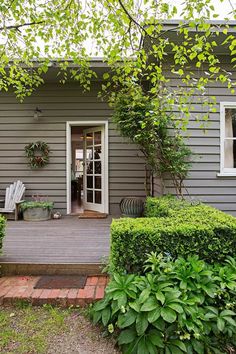 a gray house with white trim and wooden steps leading up to the front door is surrounded by greenery