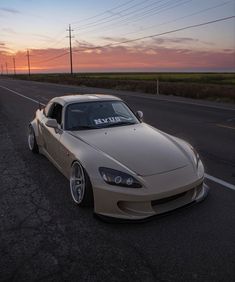 a tan sports car parked on the side of the road at sunset with power lines in the background