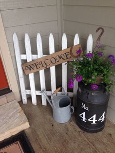 a white picket fence sitting next to a potted plant and watering can on a porch