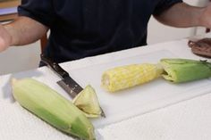 a man cutting up corn on the cob with a knife and other food items