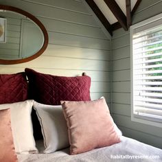 a bed with pink and white pillows next to a wooden mirror on top of the headboard