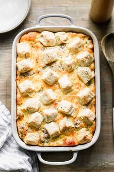 a casserole dish with chicken and cheese in it on a wooden table next to utensils