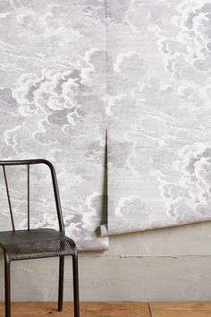 a chair sitting on top of a wooden floor next to a wall with clouds painted on it