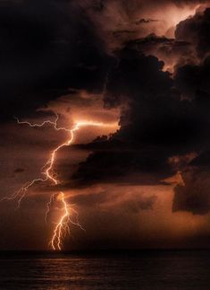 a large cloud filled with lots of lightning in the night sky over water and land