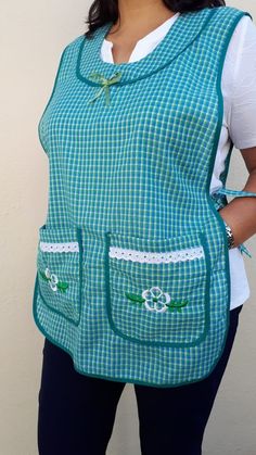 a woman wearing a blue and white checkered apron with pockets on the front, standing in front of a wall