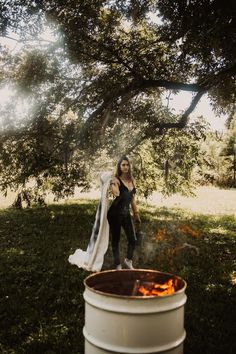 a woman standing in the grass next to a barrel with fire coming out of it