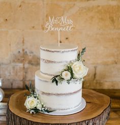 a wedding cake with white flowers and a mr and mrs sign on top is sitting on a tree stump