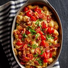 a casserole dish with tomatoes and parsley in it on a striped cloth