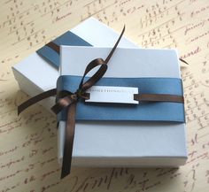 two white boxes with blue and brown ribbons tied around each other on top of a table