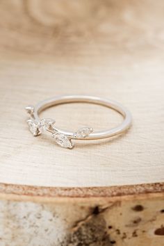 a silver ring sitting on top of a piece of wood with two small leaves sticking out of it