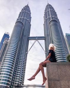 a woman is sitting on a ledge in front of two very tall buildings with their legs crossed