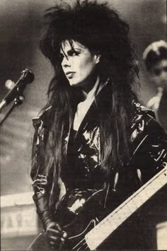 an old black and white photo of a woman with long hair holding a guitar in front of a microphone