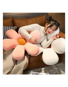 a woman laying on top of a couch covered in giant pillows and holding a flower shaped pillow