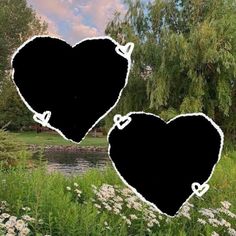 two black heart shaped stickers sitting on top of a lush green field next to a river