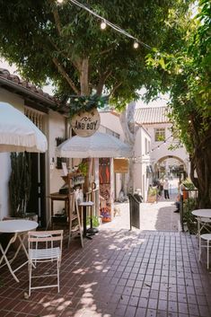 an alley way with tables and chairs under umbrellas on the side walk, surrounded by trees