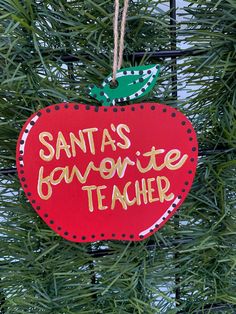 a christmas ornament hanging from a tree with santa's favorite teacher written on it