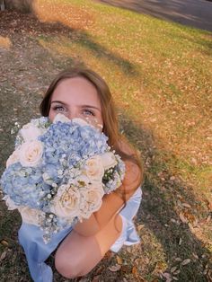 a woman holding a bouquet of blue and white flowers in front of her face while looking at the camera