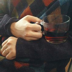 a person wearing a sweater and holding a coffee cup with both hands on their arm