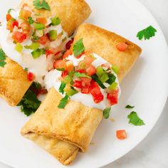 three mexican pastries on a white plate with cilantro and sour cream sauce