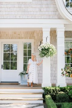 a woman standing on the steps with flowers in front of a house and holding a bucket