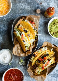 three tacos with toppings and condiments on the side, including guacamole