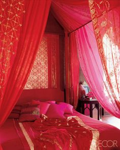 a bed with red sheets and pink curtains