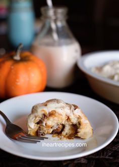 a white plate topped with a pastry covered in icing next to two small pumpkins